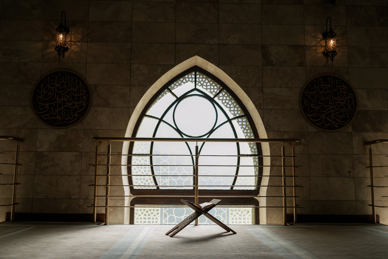 A peaceful mosque interior featuring a backlit window, rehal stand, and intricate architecture.